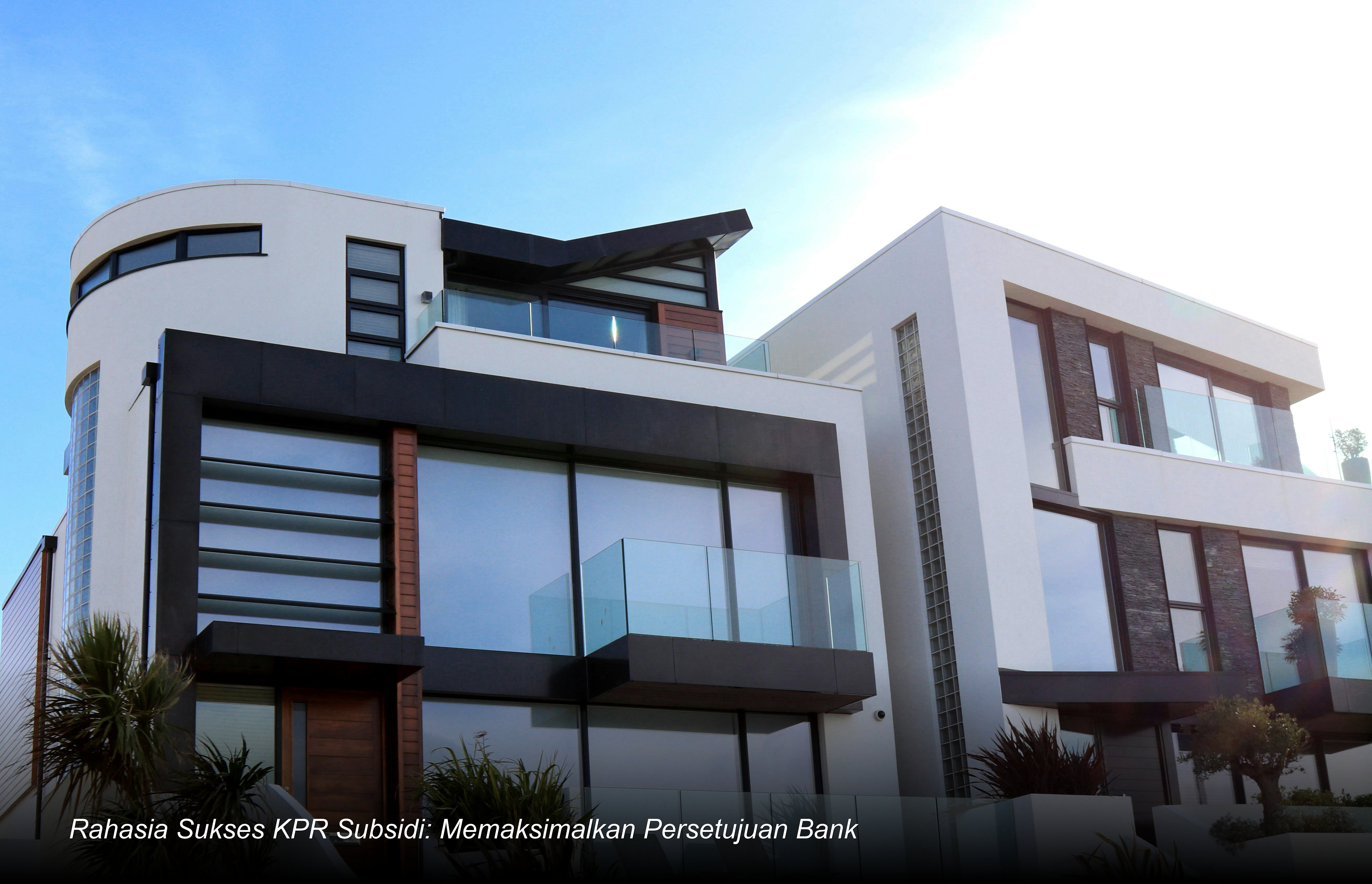 Seorang pasangan muda tersenyum bahagia saat menandatangani dokumen akad kredit KPR di hadapan petugas bank dengan latar belakang miniatur rumah minimalis modern.